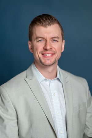 Business professional in light gray suit jacket and white shirt against blue background.