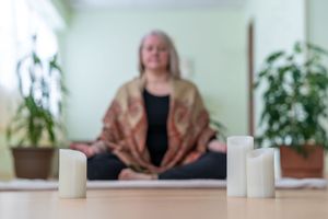 Meditation scene with candles and blurred figure in lotus pose against green plants.