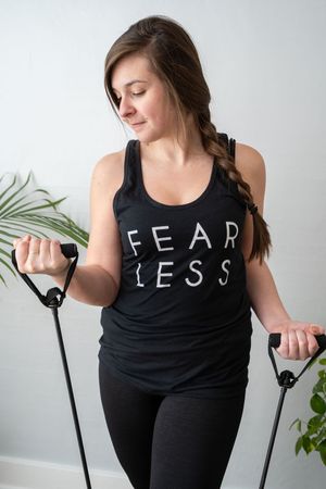Woman in black Fearless tank top using exercise resistance bands.