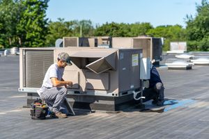 Technician performing maintenance on a commercial HVAC unit on a rooftop.