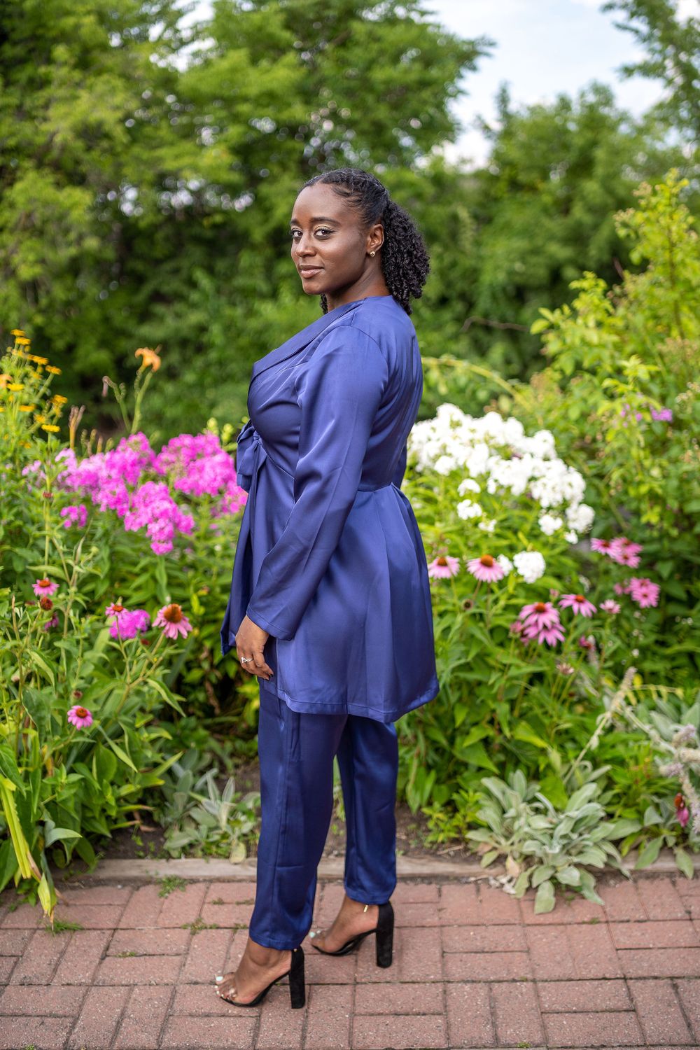 Woman in navy blue outfit posing in a colorful garden with pink flowers.