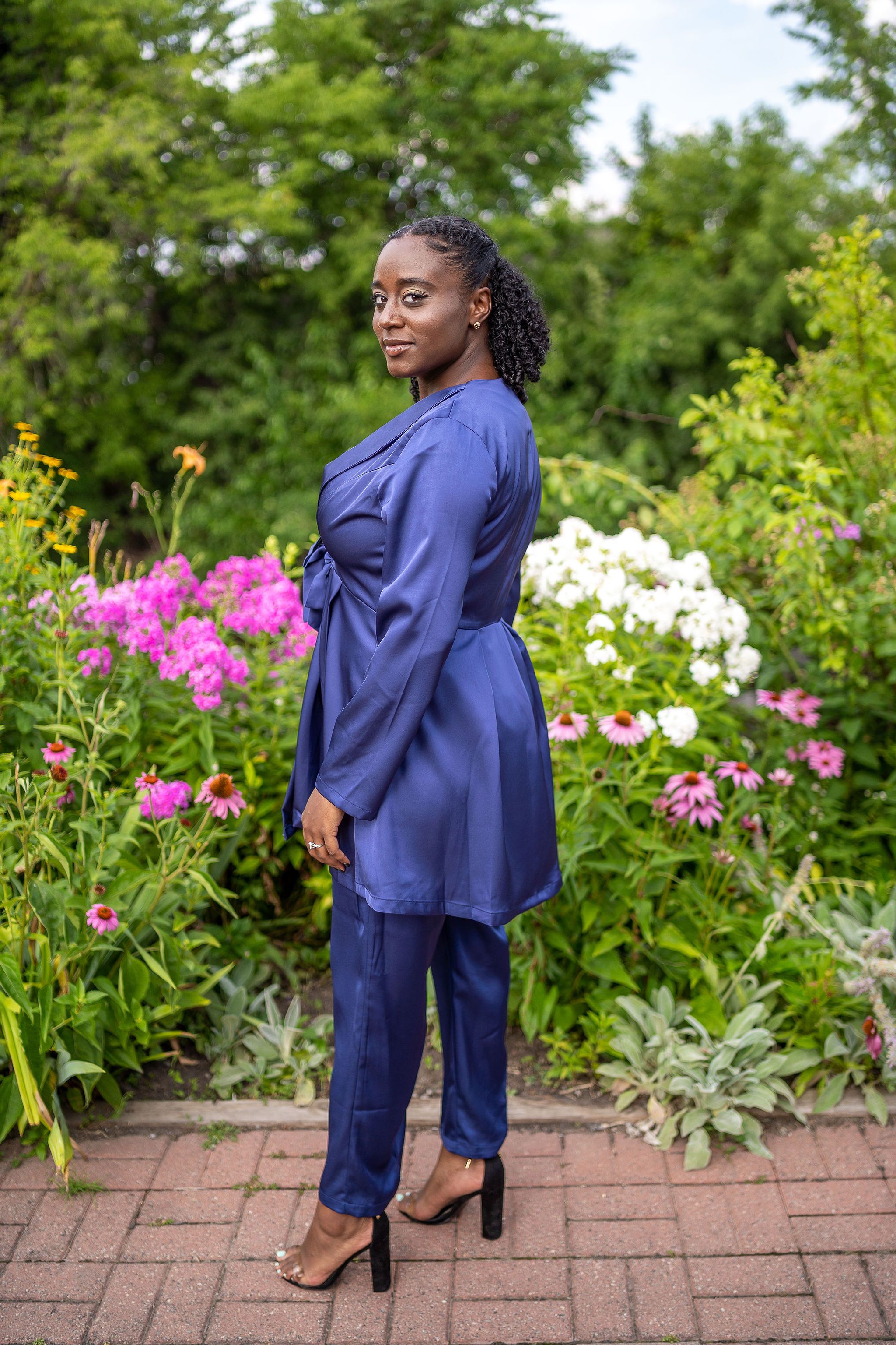Woman in navy blue outfit posing in a colorful garden with pink flowers.