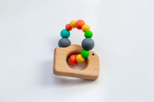 Colorful wooden baby teething toy with rainbow beads on white background.
