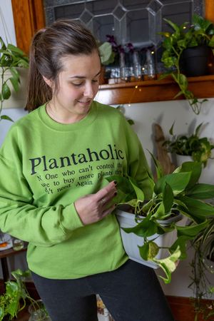 Person wearing bright green Plantaholic sweatshirt holding a houseplant.