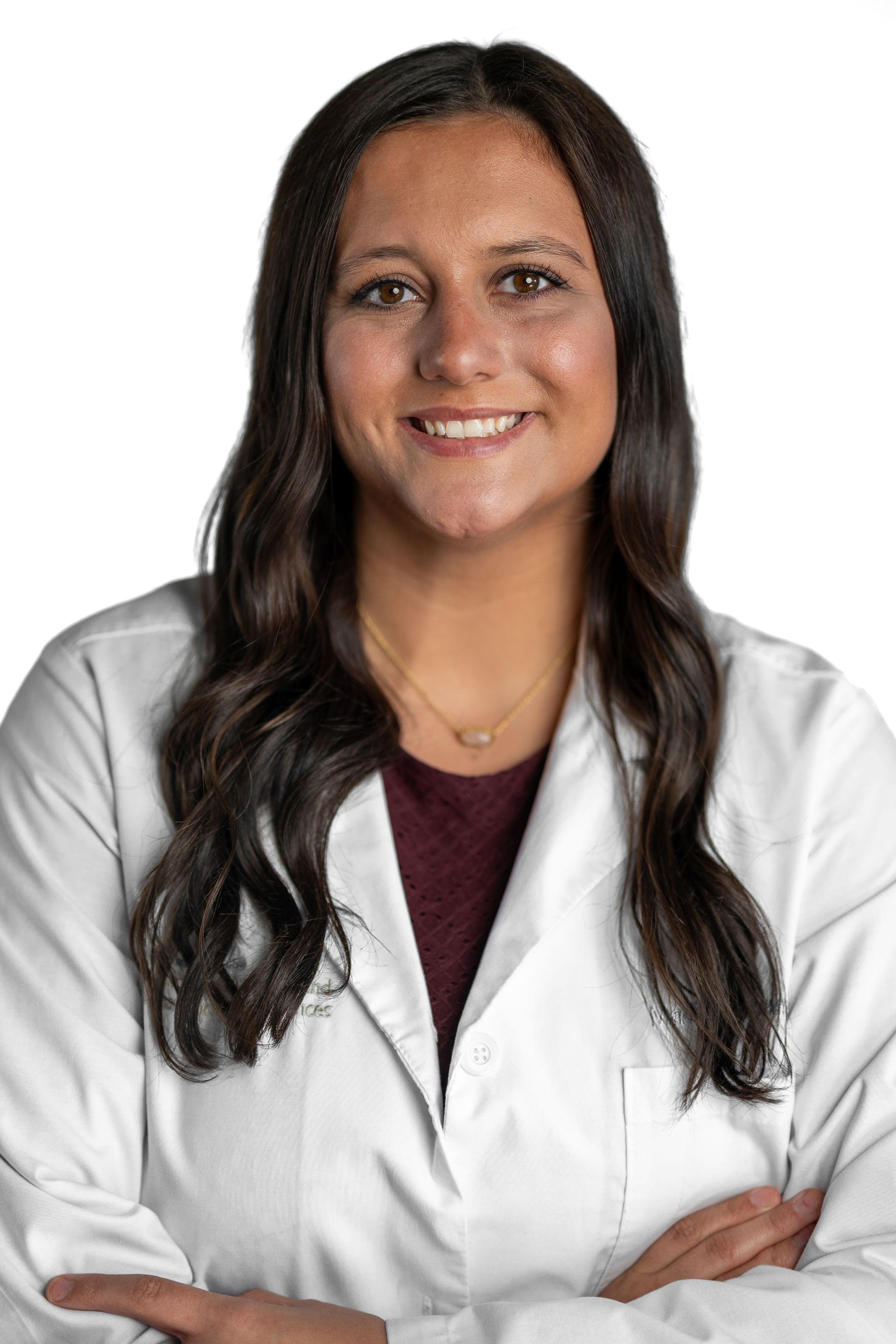 Healthcare professional in white coat and burgundy top smiling with arms crossed.