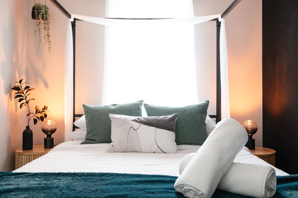 Modern canopy bed with teal and white bedding and ambient lighting.
