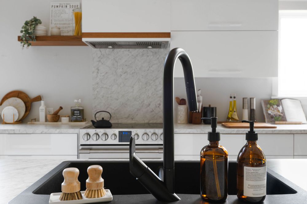 Minimalist white kitchen with matte black faucet, wooden shelf, and marble backsplash.