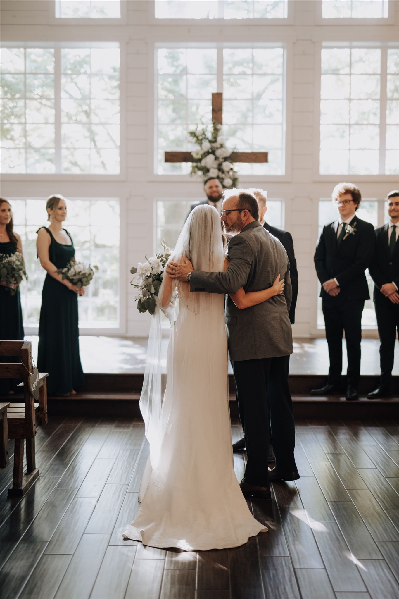 A wedding ceremony embrace in front of a cross-adorned altar with floral decorations.