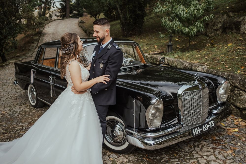 Carro clássico Mercedes-Benz preto com um casal em trajes de casamento a posar ao lado.