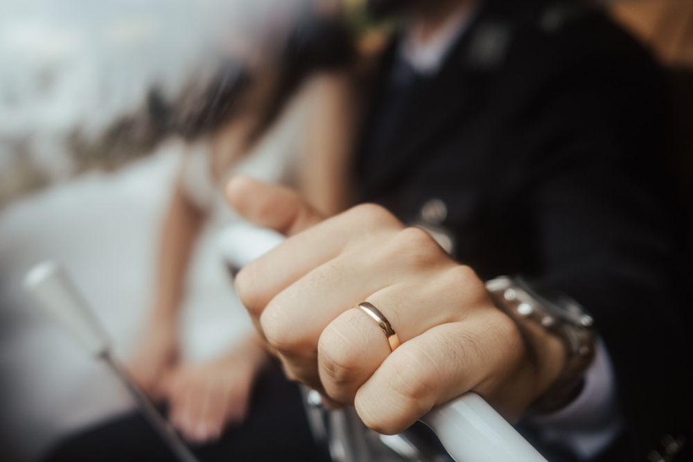 Fotografia de grande plano de uma aliança de casamento em ouro numa mão apoiada no teclado de um piano.