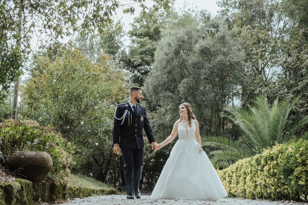 Casal de noivos a caminhar por um trilho no jardim, rodeado por vegetação exuberante.