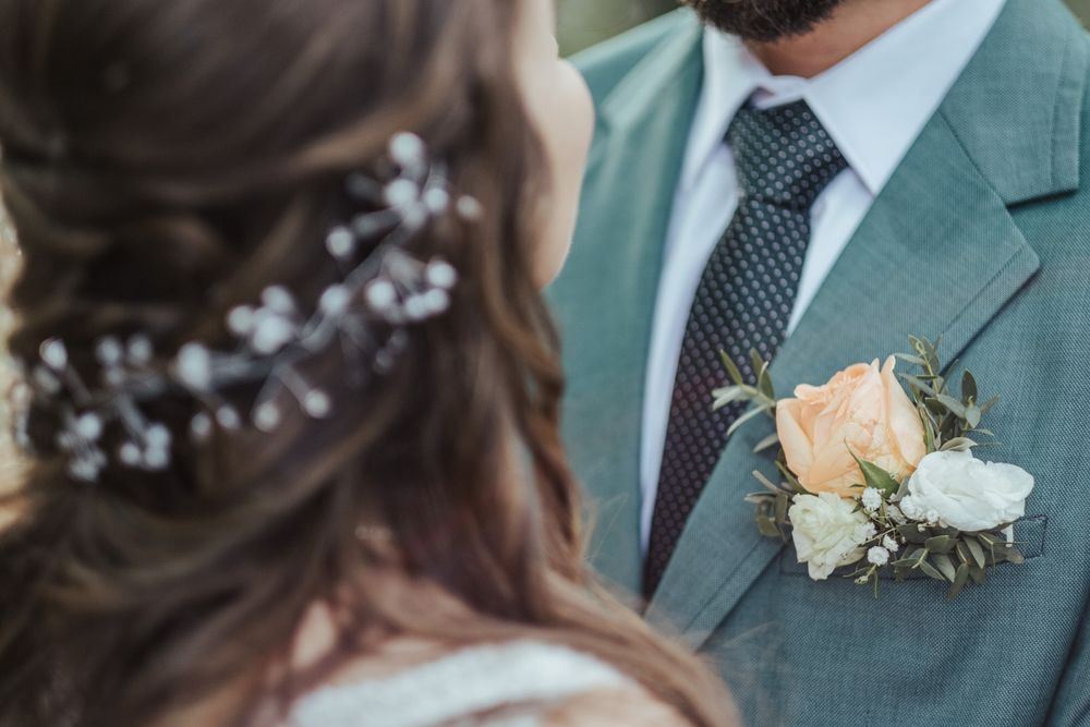 Pormenor de um fato verde-sálvia com uma rosa branca na lapela e delicados acessórios de cabelo.
