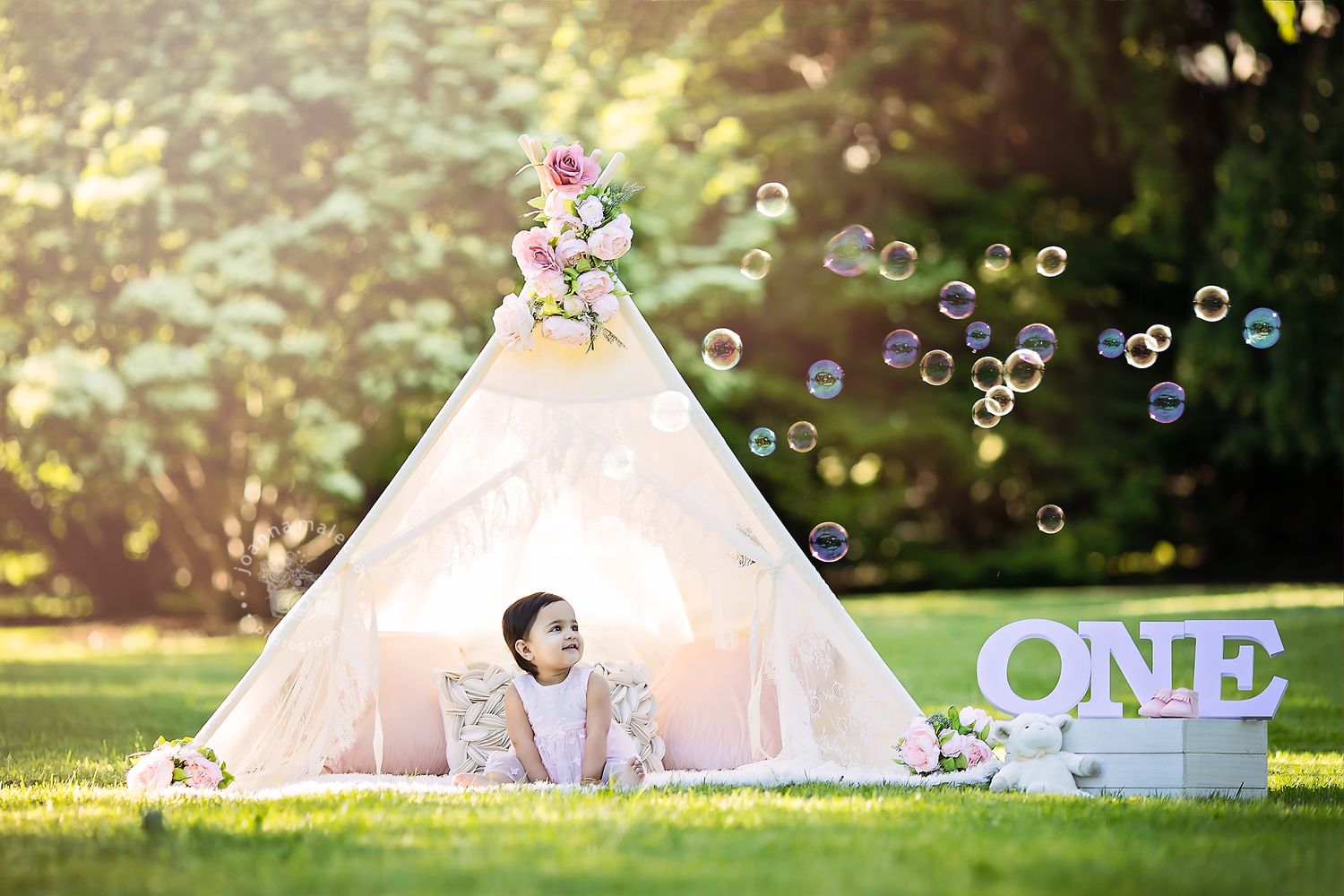 Baby girl sitting inside a white teepee tent with bubbles and ONE sign in garden.