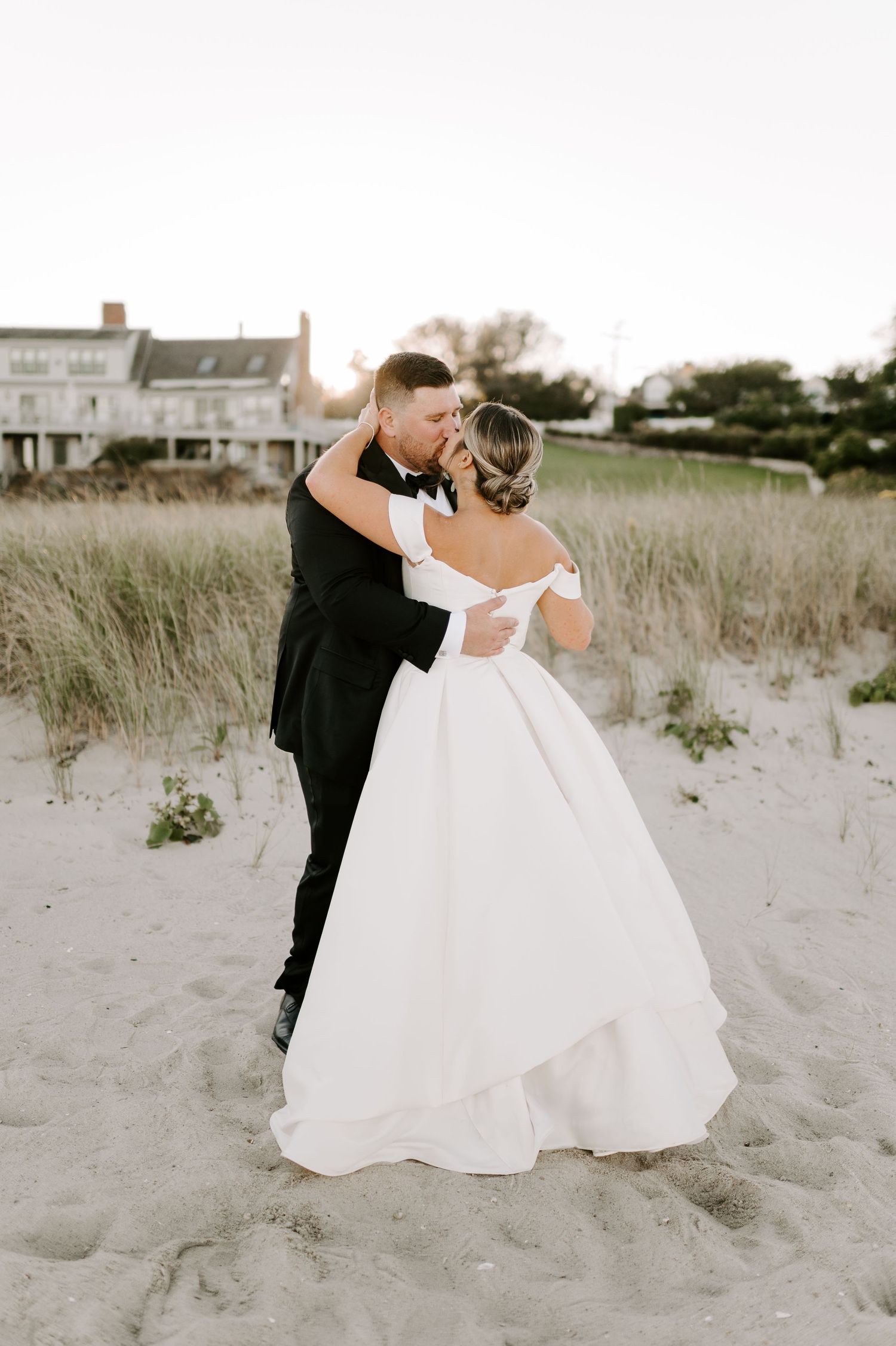 Romantic wedding couple shares intimate moments on sandy beach with coastal vegetation.