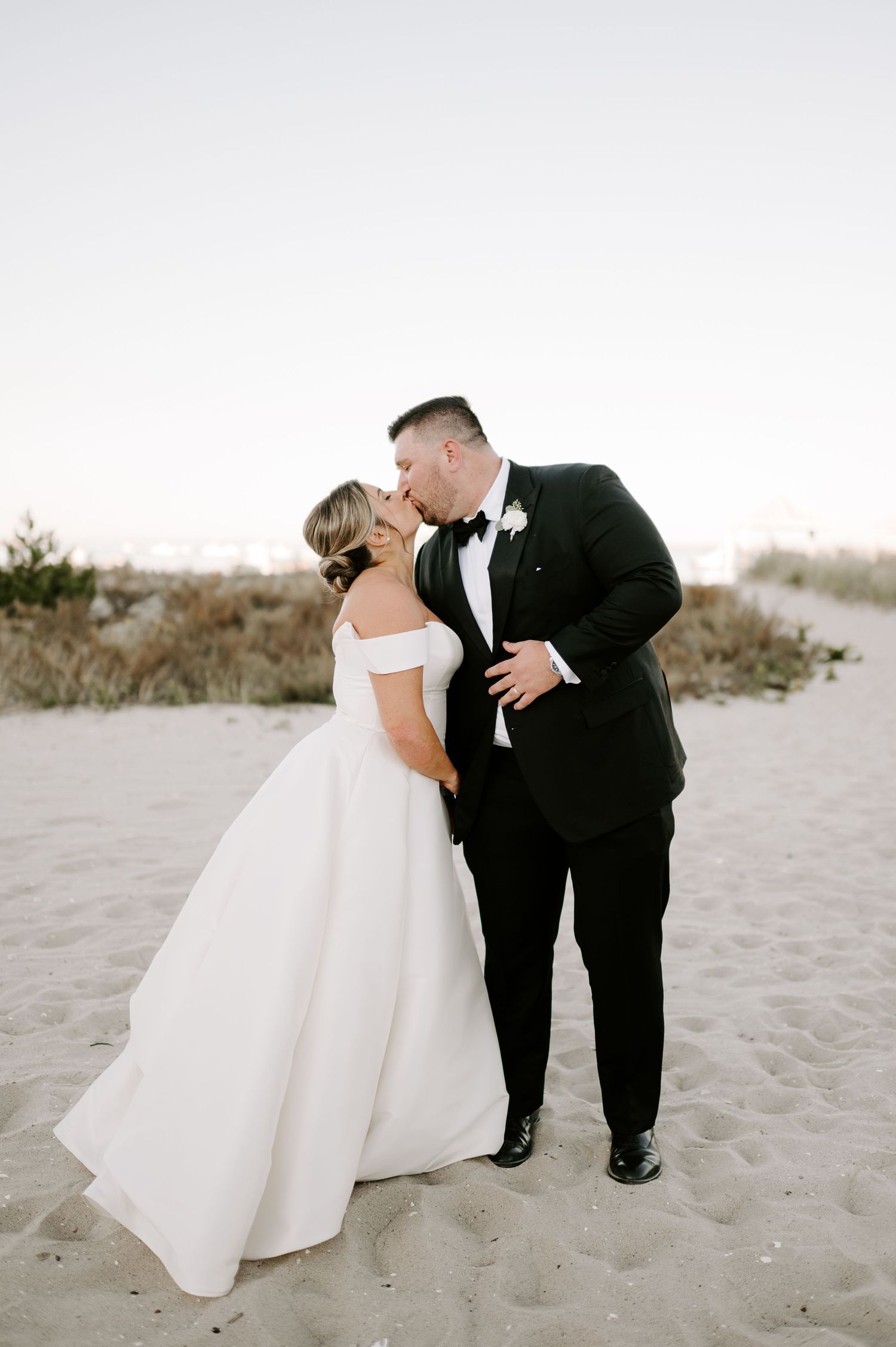 Wedding couple shares romantic moments during a beach photoshoot with soft lighting.