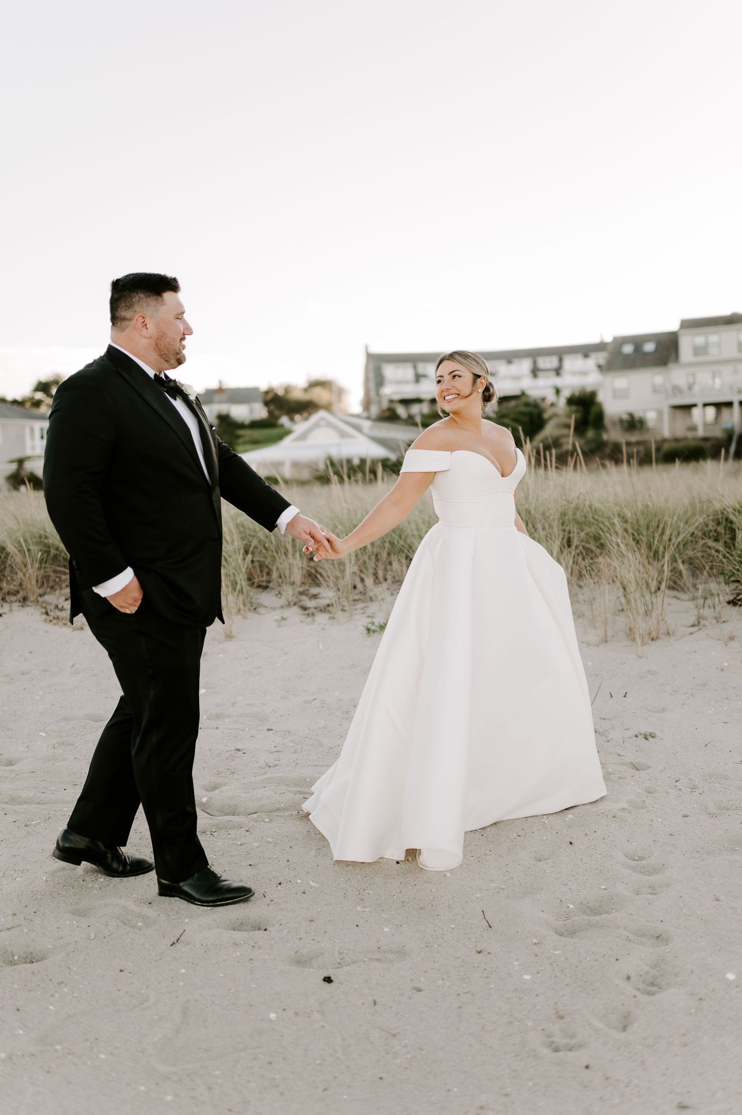 Bride and groom dance playfully on sandy dunes during their beach wedding photo session.
