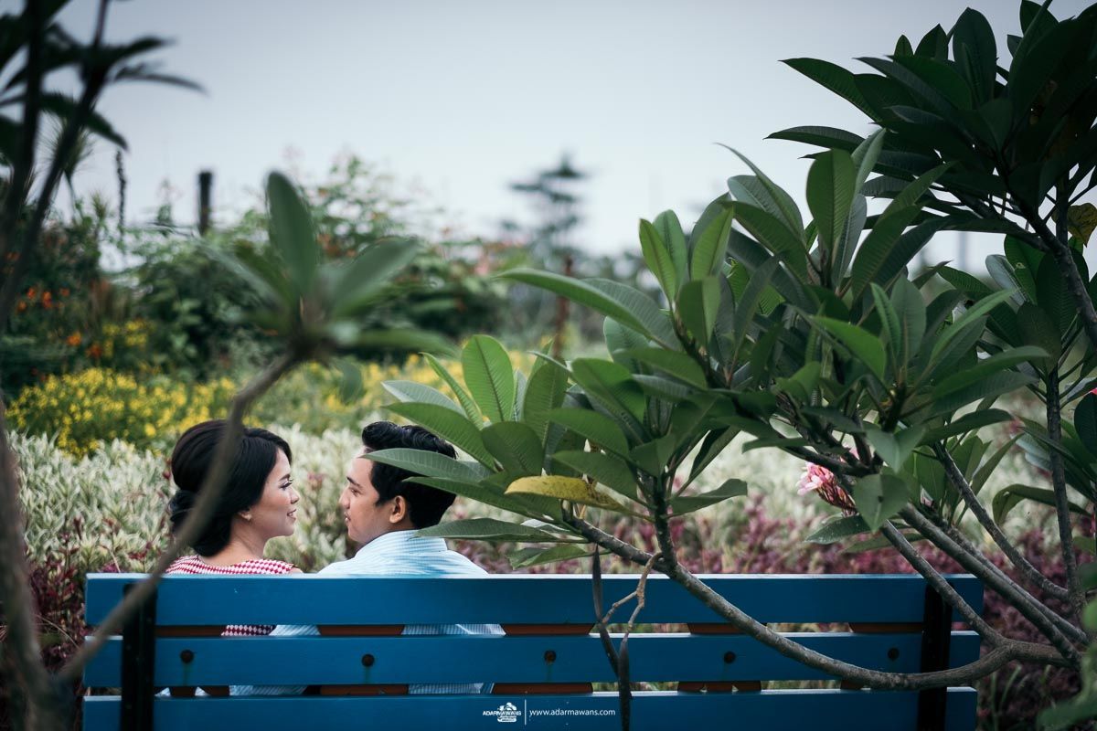 A couple sitting together on a blue bench surrounded by tropical plants and palm trees.
