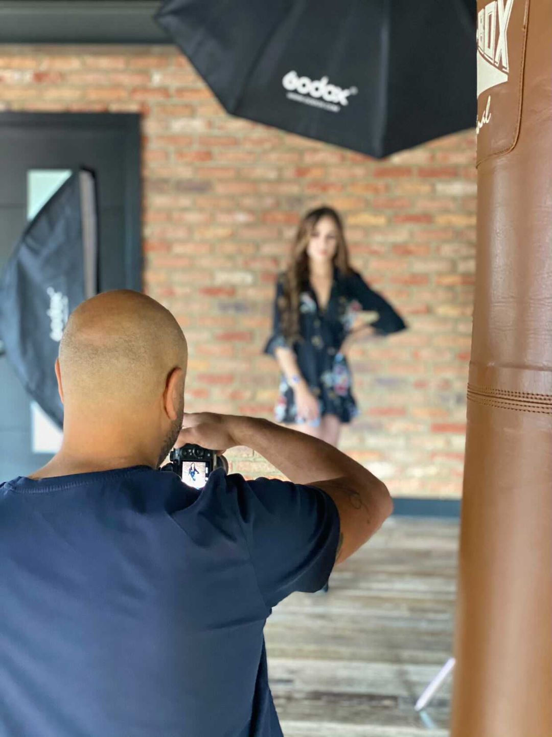 Behind-the-scenes photo of photographer shooting model in studio with lighting equipment visible.
