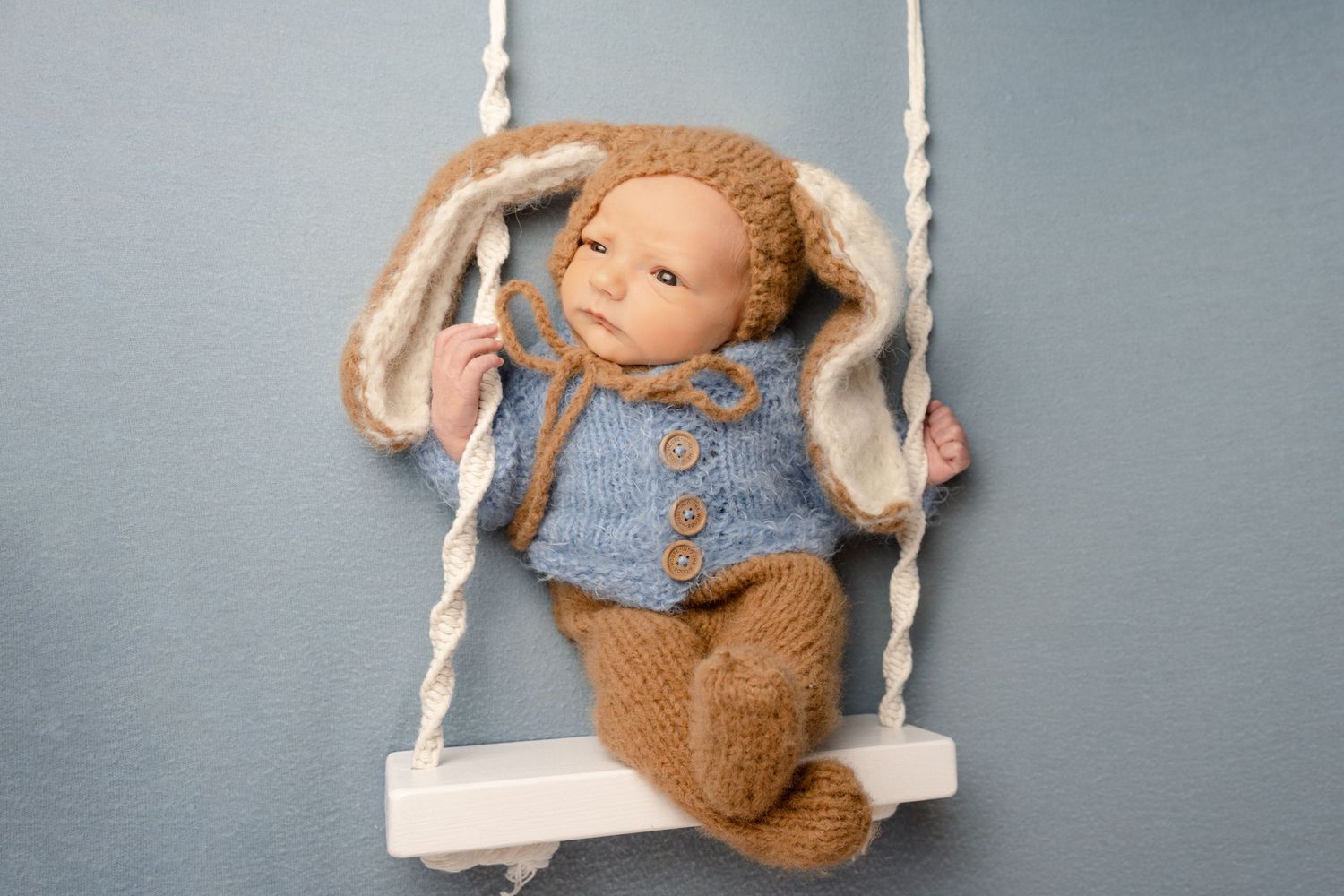 Newborn baby wide awake wearing a peter rabbit outfit whilst sat on a swing prop during newborn photoshoot in Doncaster.
