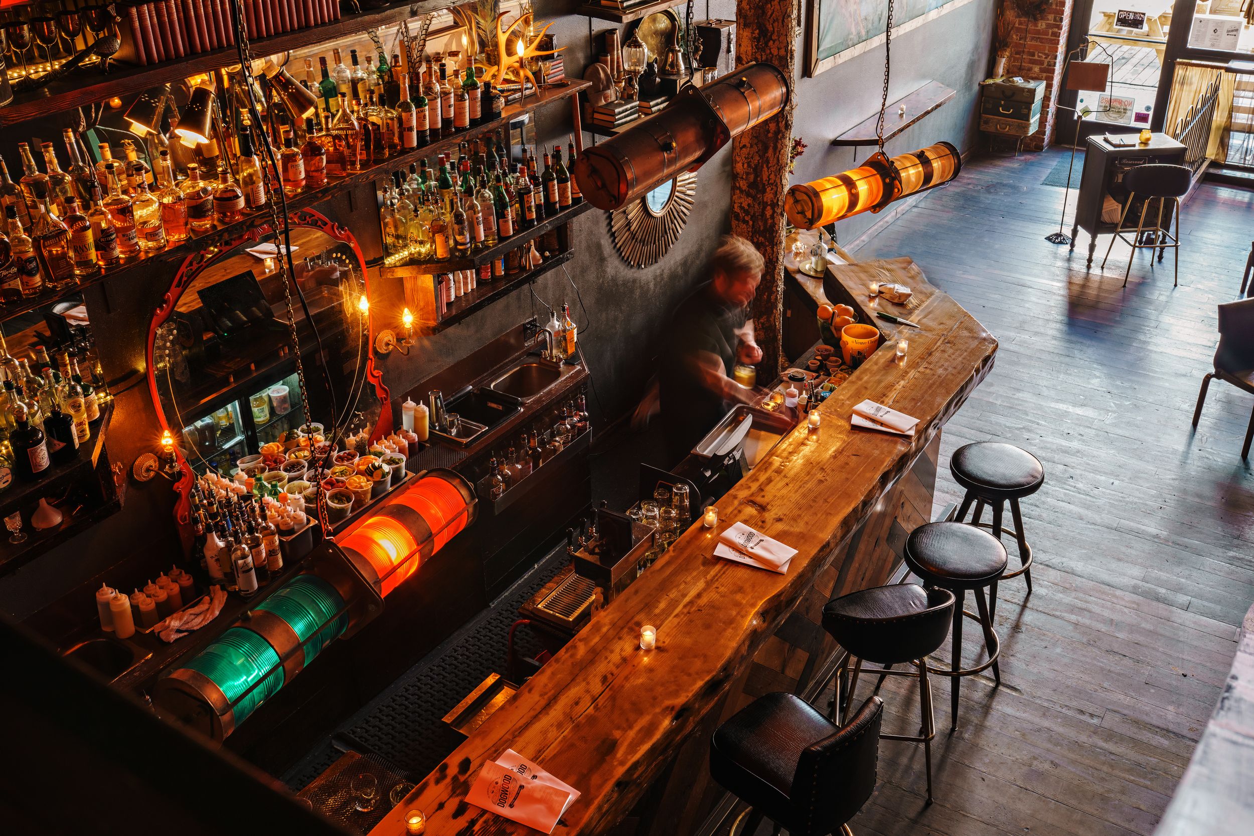 Rustic bar counter with wooden top and stools illuminated by warm ambient lighting.
