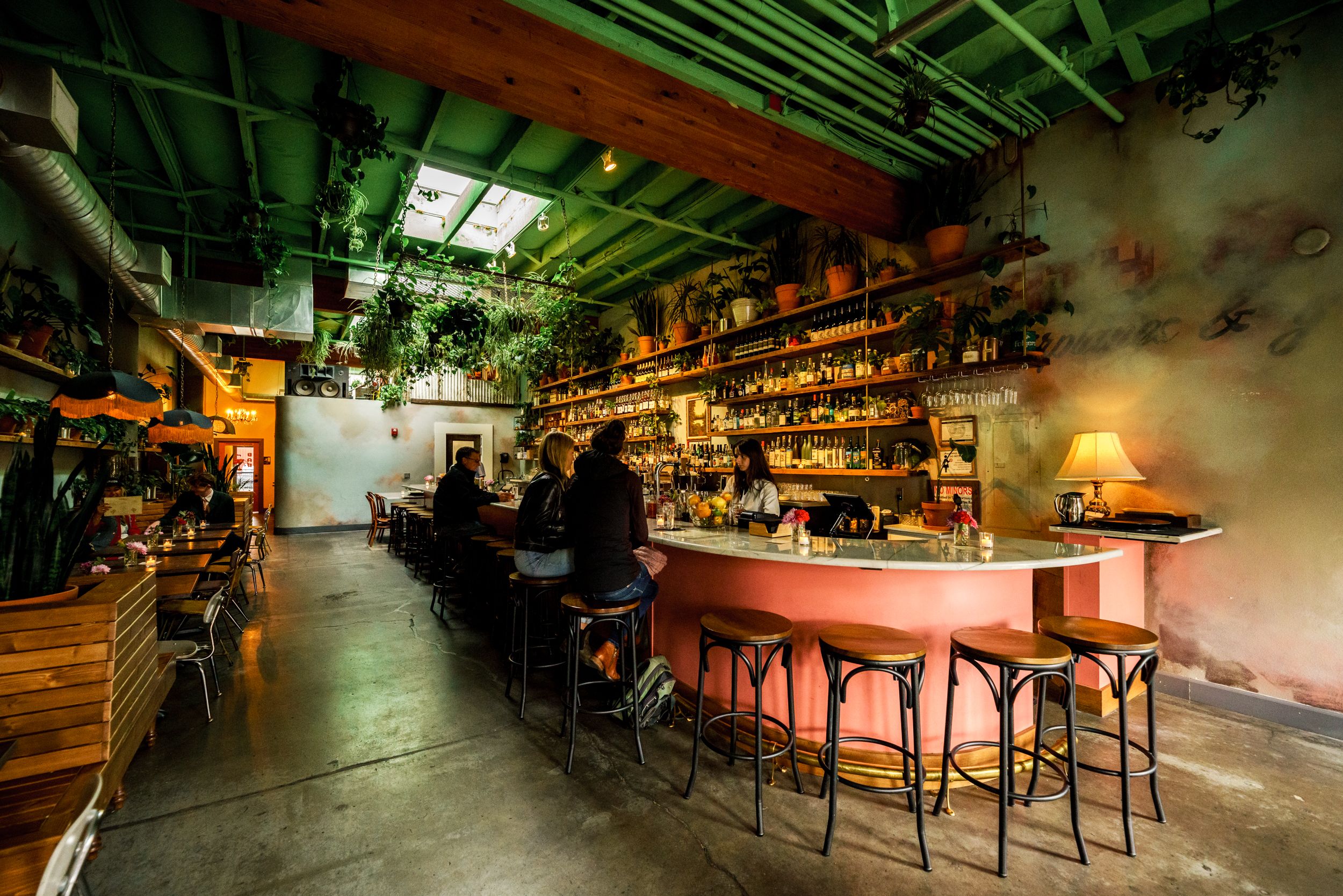 Industrial-style bar with exposed ceiling and glowing shelves of bottles.