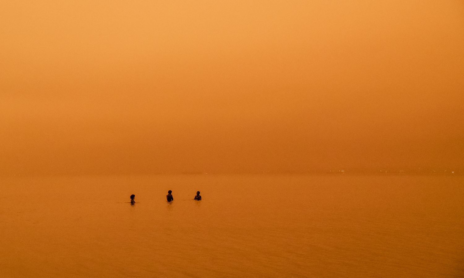 Three boys playing in the ocean under an orange sky