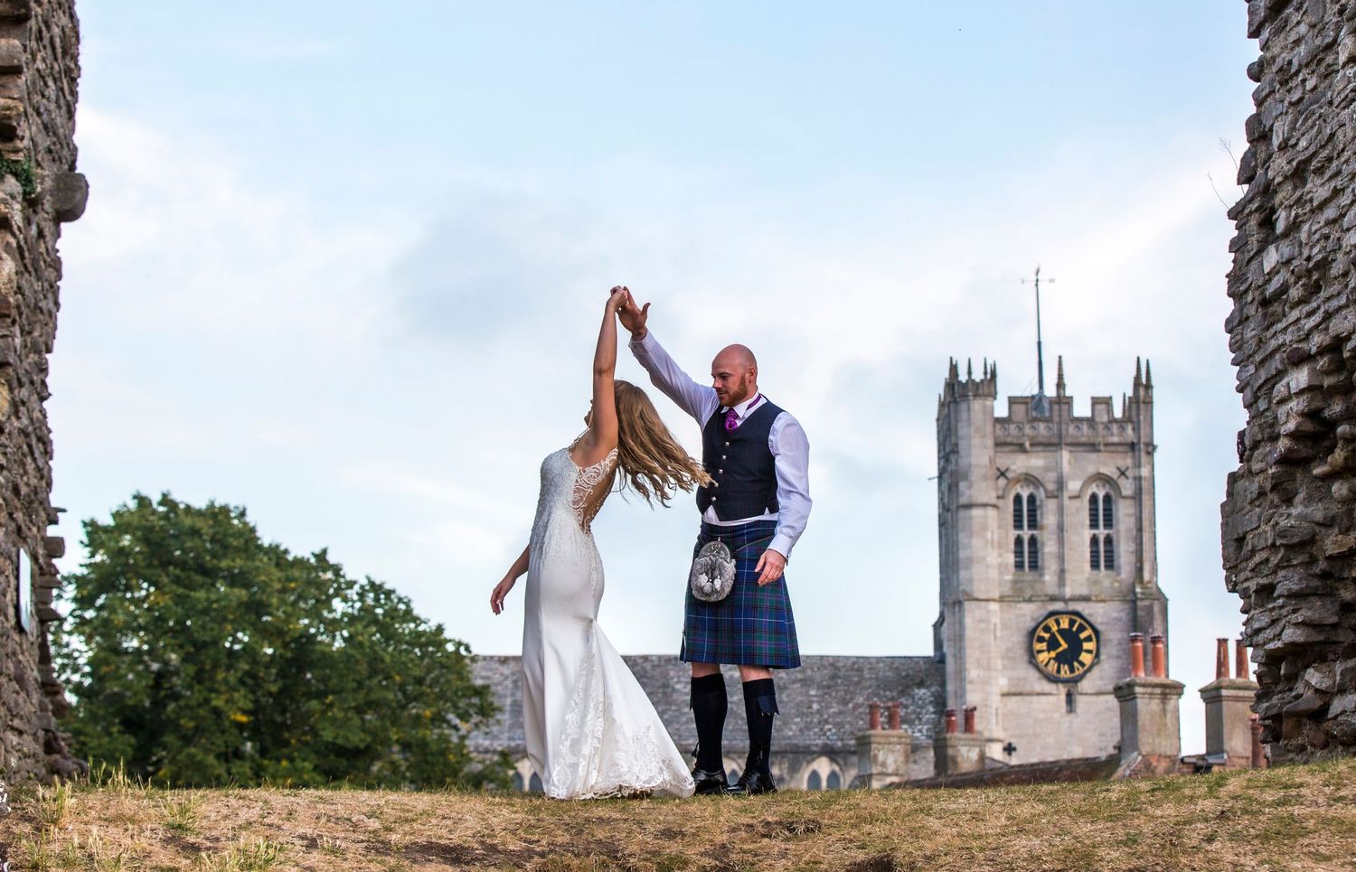 Panoramic wedding portrait with medieval church architecture in the distance.