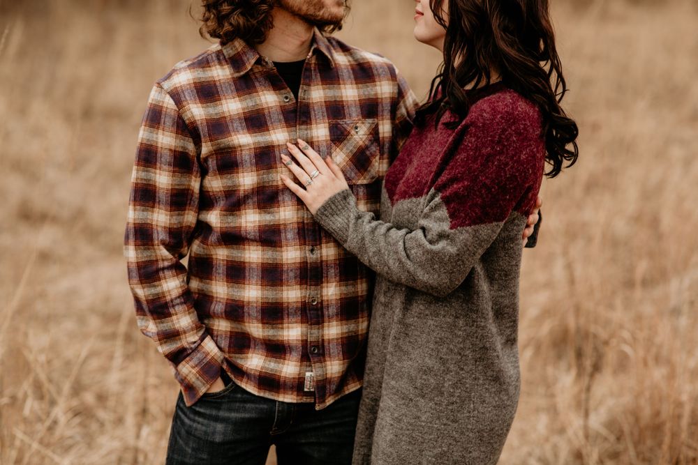 Close-up of couple embracing in golden autumn field, woman in gray and burgundy sweater placing hand on mans chest.