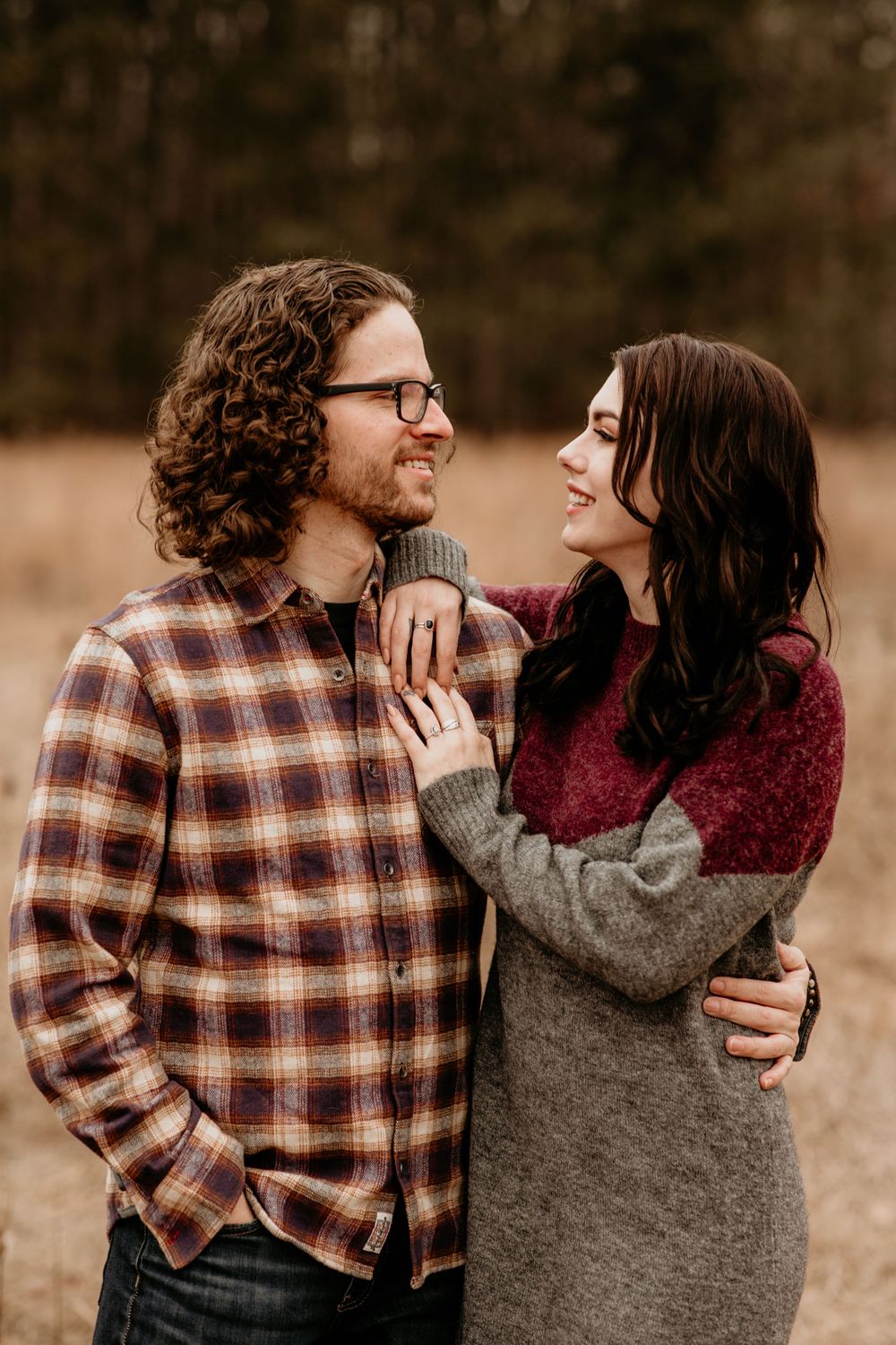 Couple sharing a tender smile in golden autumn meadow, man in plaid shirt and woman in colorblock sweater embracing.