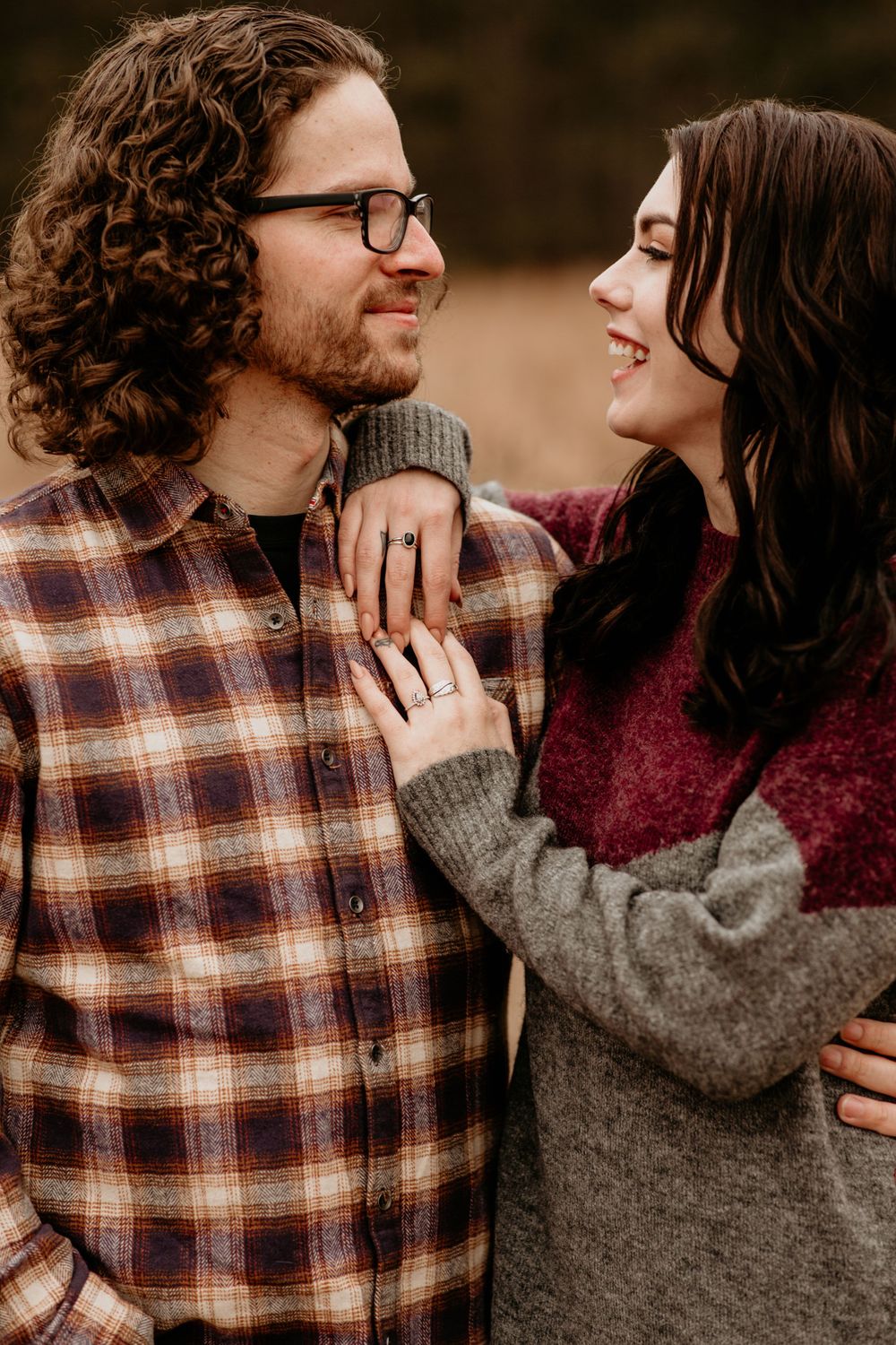 Close-up of happy couple gazing at each other in autumn setting, woman showing engagement ring on mans plaid shirt.