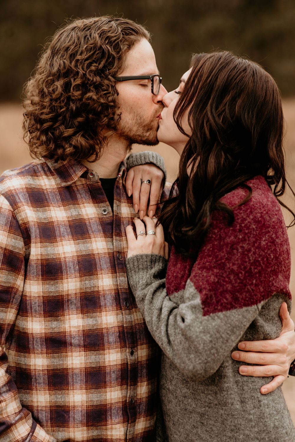 Couple sharing a passionate kiss in autumn meadow, woman in gray burgundy sweater embracing man in plaid flannel shirt.