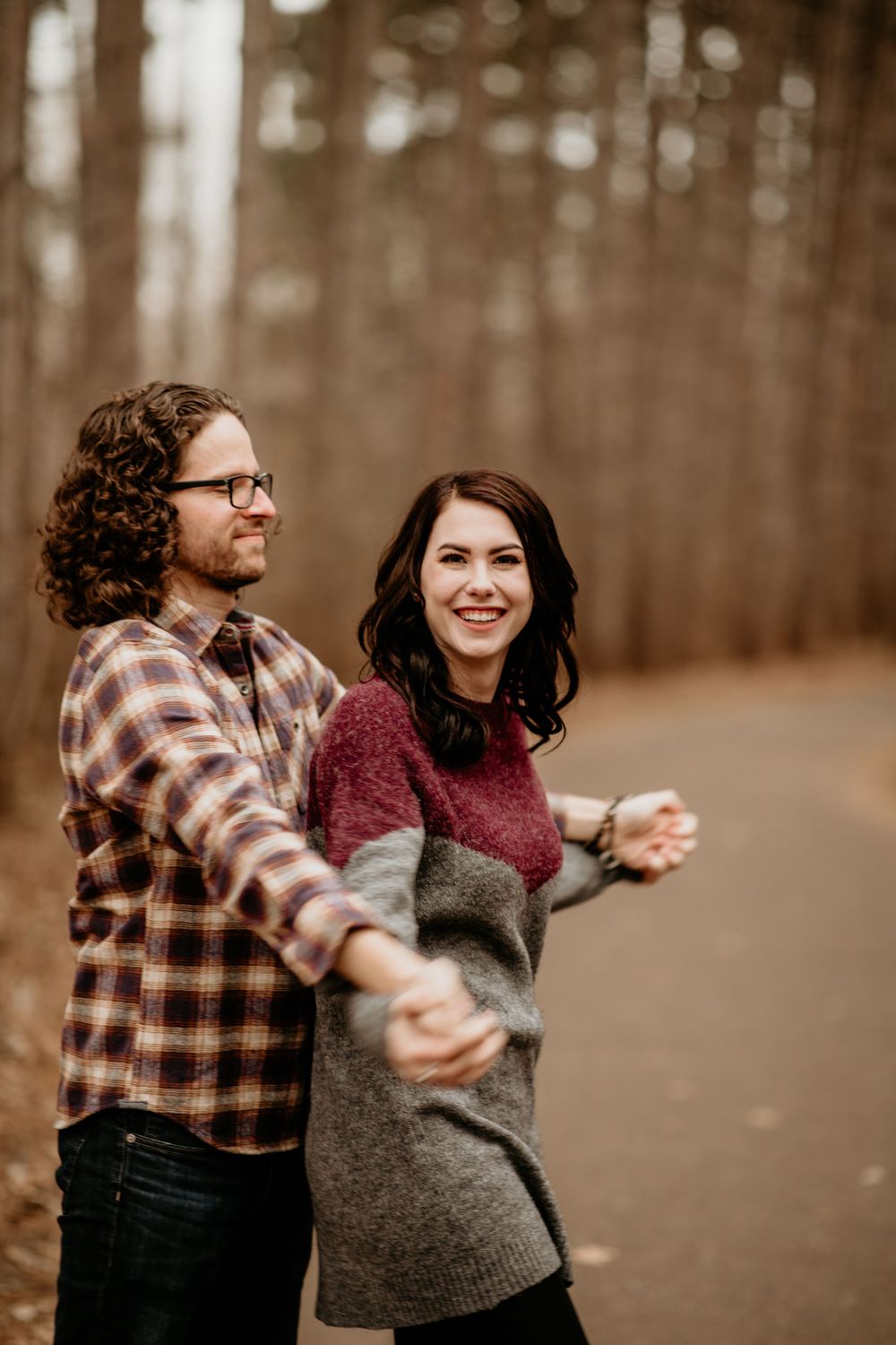 Joyful couple holding hands and walking on a tree-lined autumn path, woman smiling in colorblock sweater.