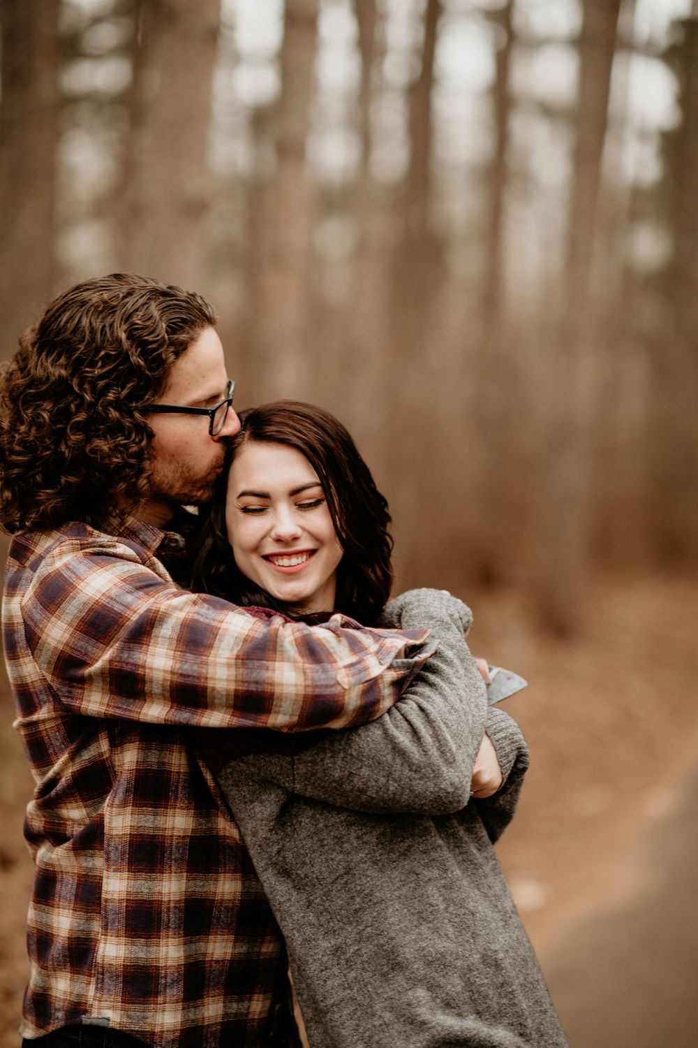 Romantic couple hugging on woodland path, man kissing smiling woman's cheek in fall setting.