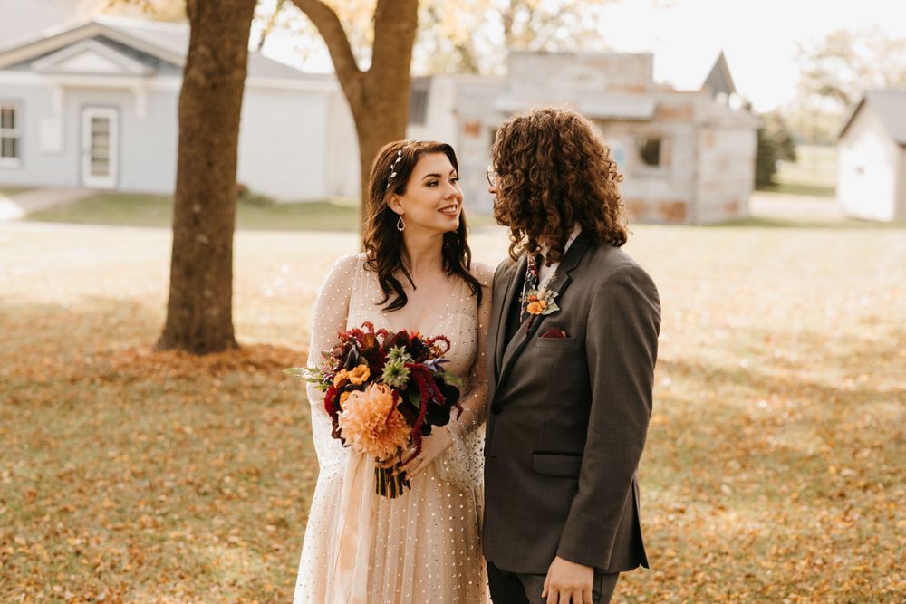 Bride and groom sharing a romantic moment outdoors among autumn fallen leaves.