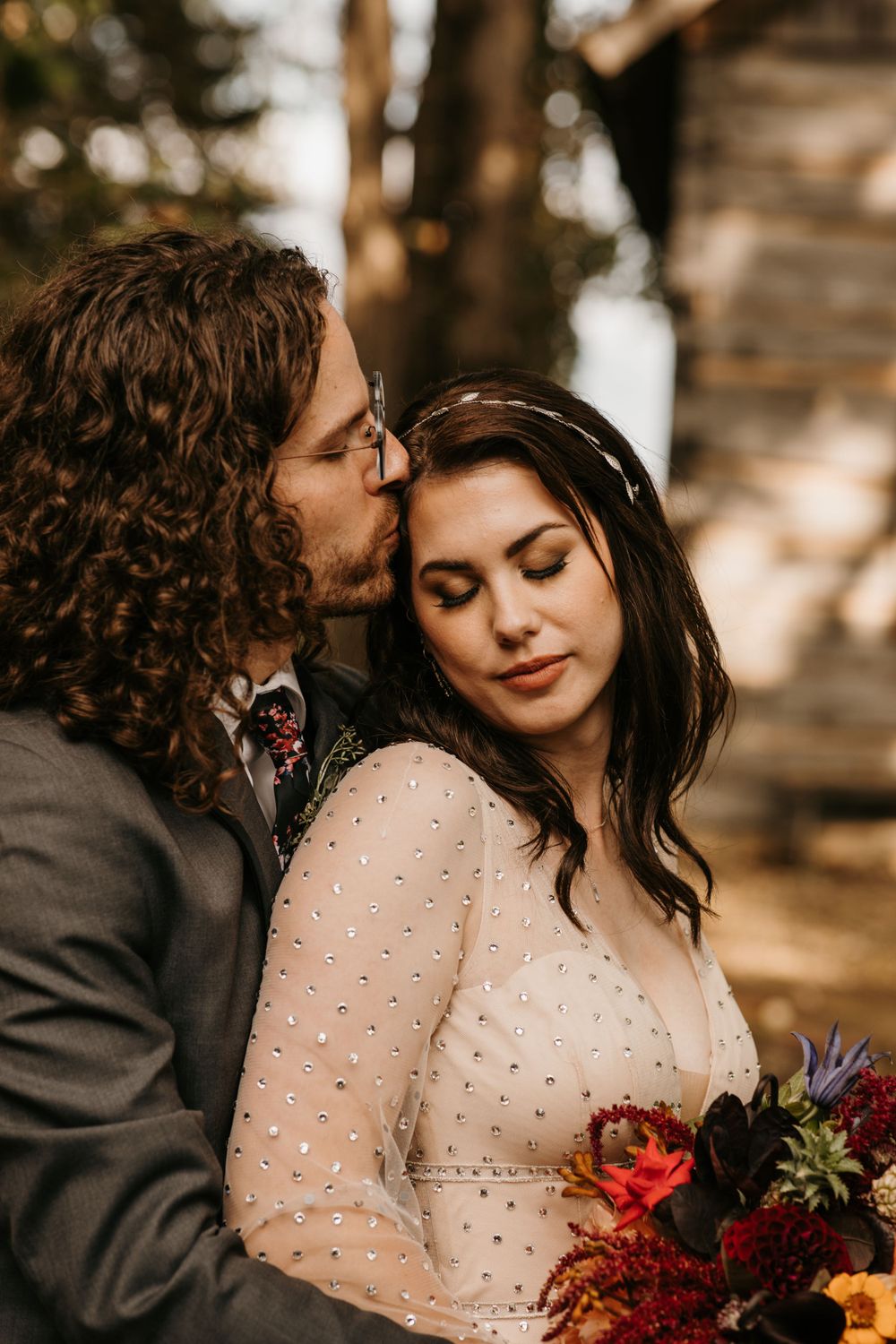 Groom tenderly kissing bride on cheek as she holds a vibrant autumn bridal bouquet.