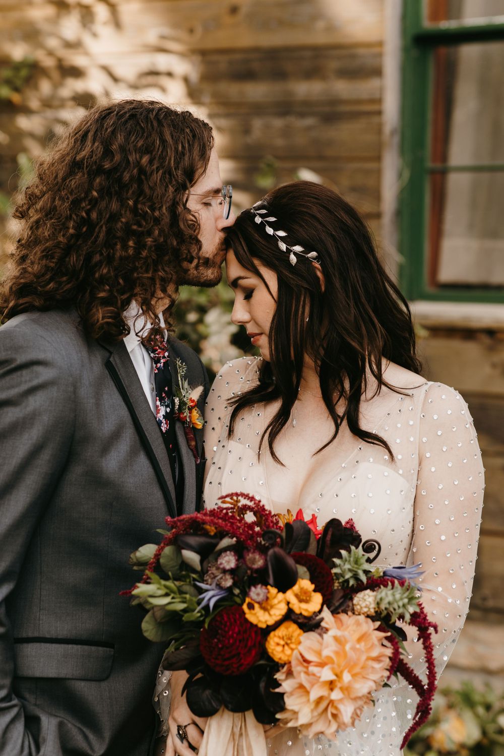 Bride and groom touching foreheads romantically holding vibrant fall wedding bouquet outdoors.