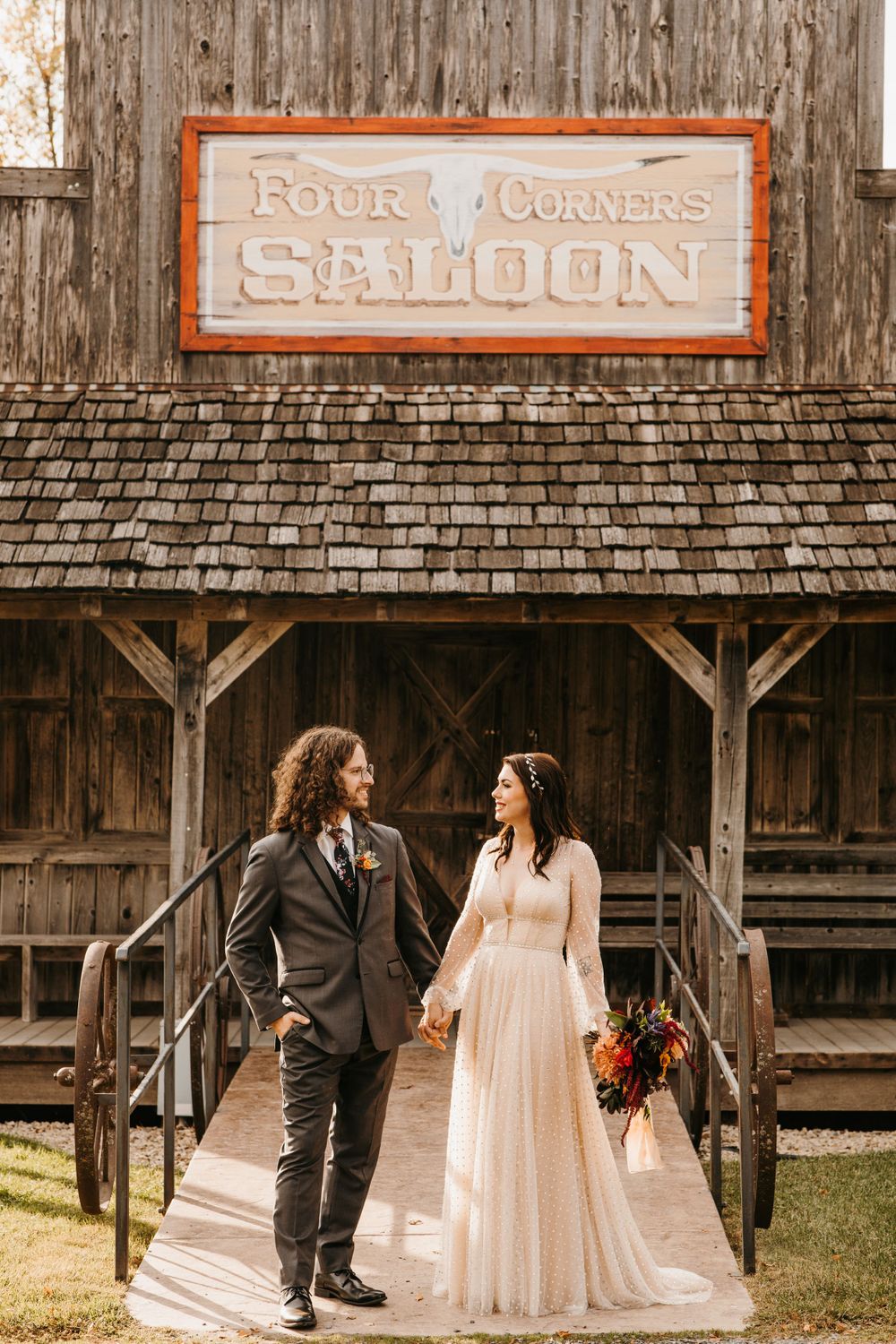 Bride and groom holding hands outside Four Corners Saloon with vibrant fall floral bouquet.