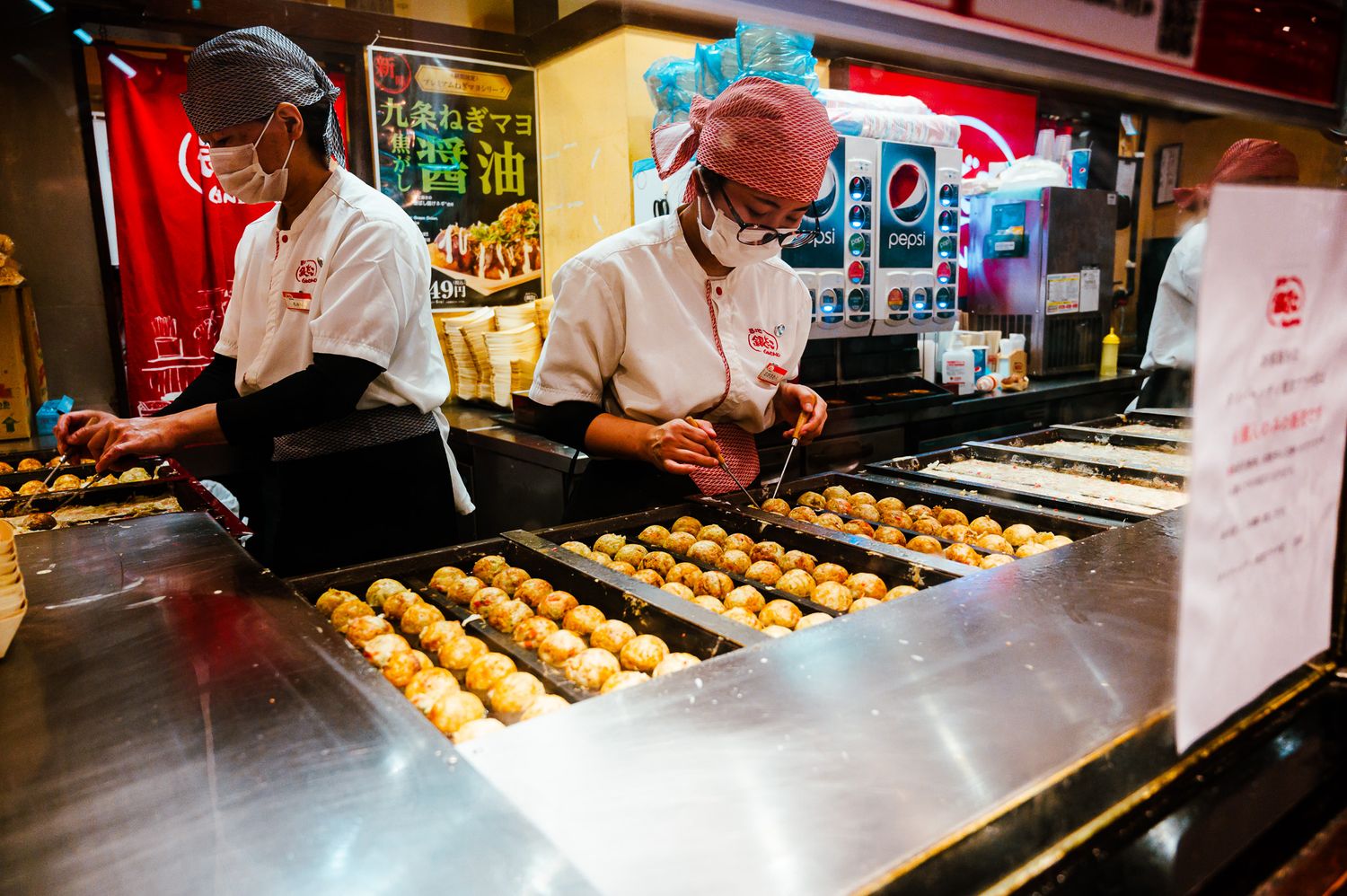 Food vendors preparing fresh takoyaki at a street market stall.