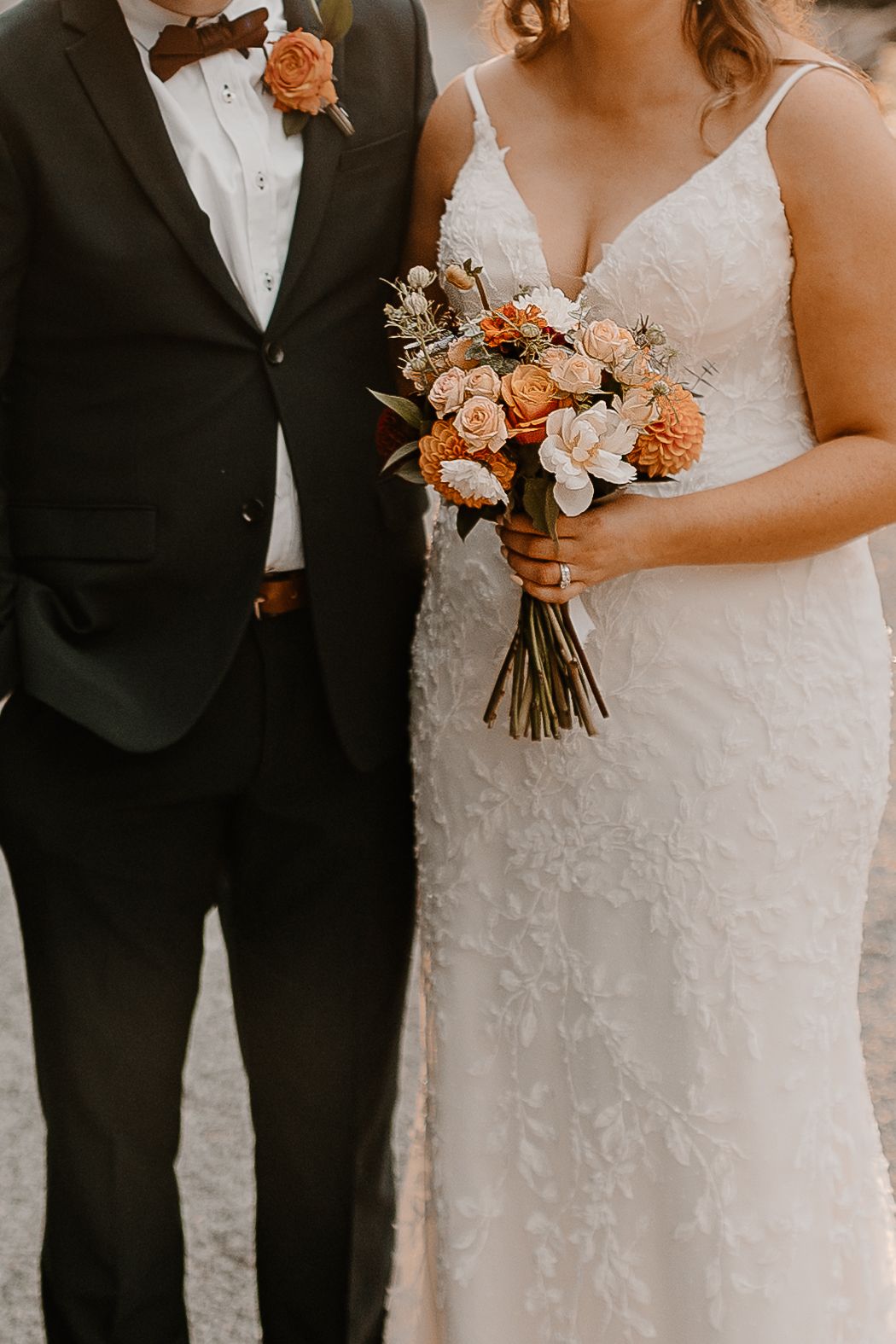 Close-up of bride and groom torsos showing formal attire and peach-toned wedding bouquet.