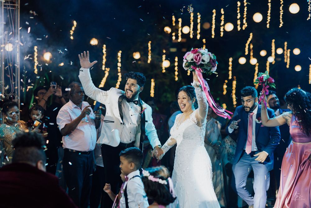 Wedding party celebrates under hanging lights and decorations during evening reception.