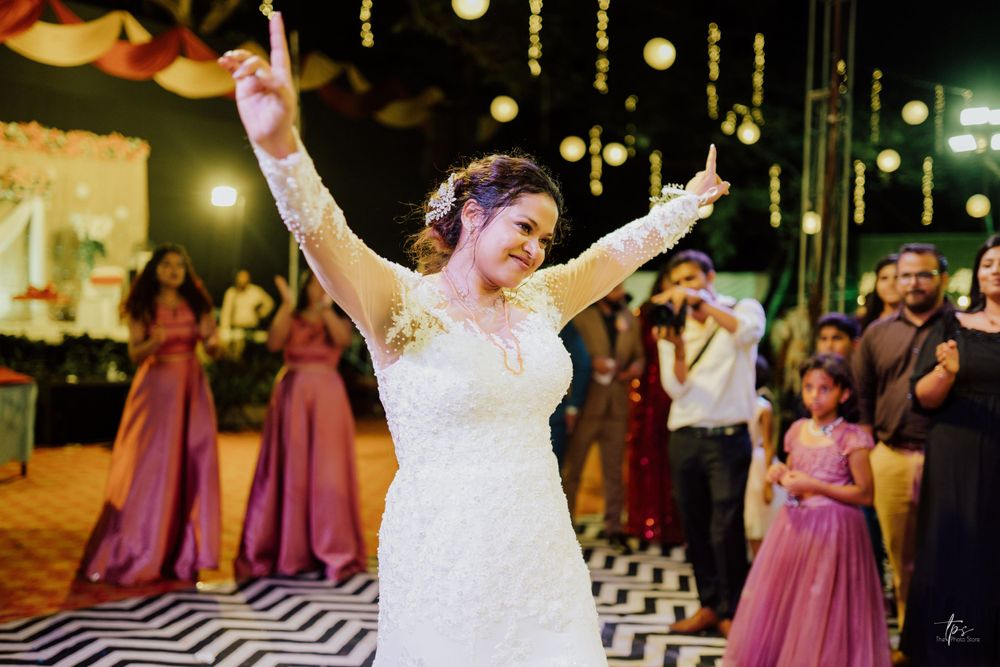 Bride in white dress dances joyfully under twinkling lights at outdoor reception.