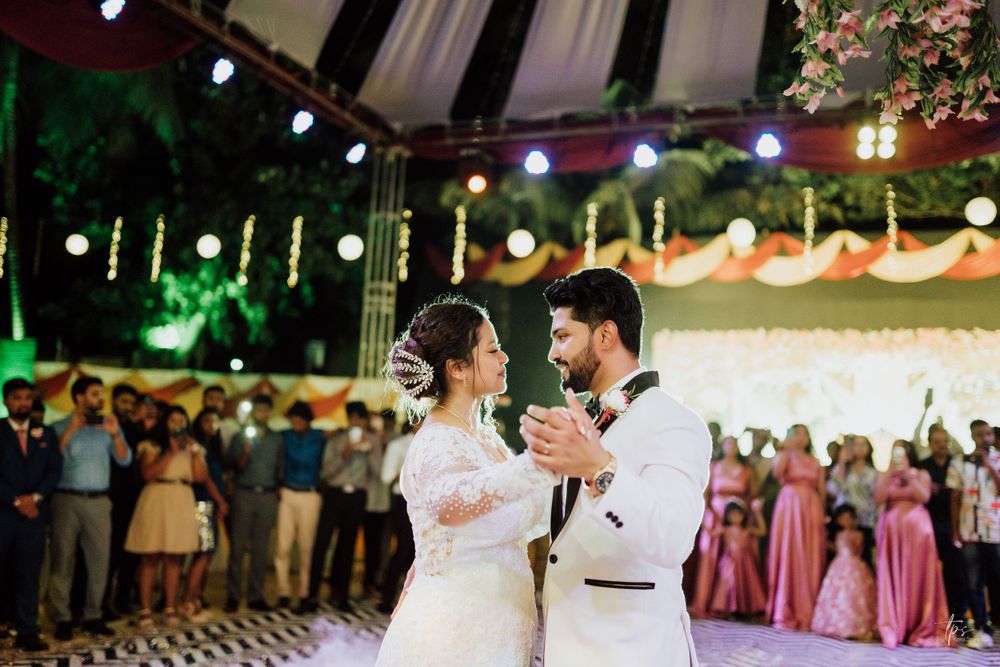 A couple shares an intimate dance moment under decorative string lights at their reception.