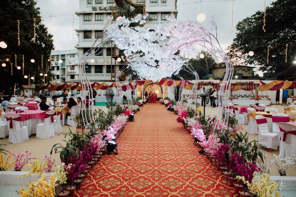 Outdoor wedding venue pathway decorated with pink flowers and string lights at dusk.