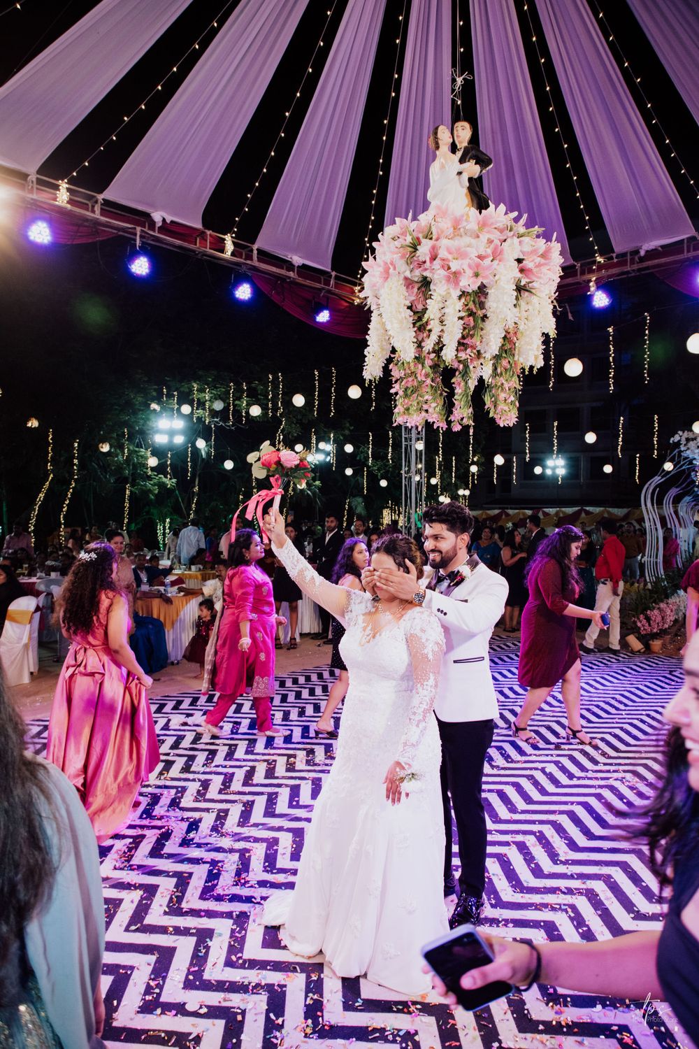 Wedding party dancing on a chevron-patterned floor under purple mood lighting and hanging decorations.