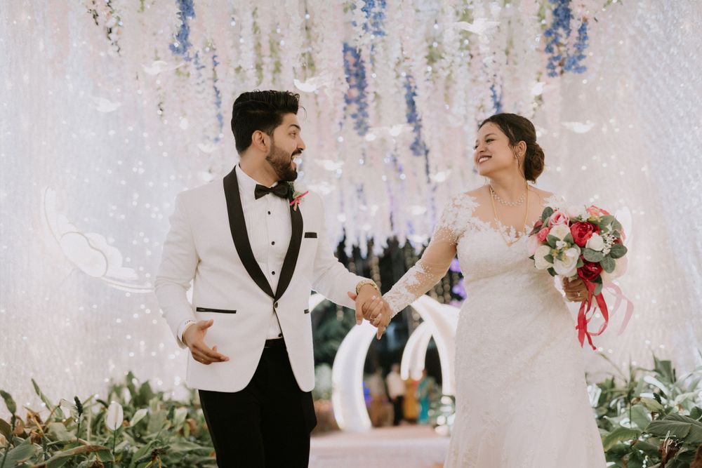 A couple shares a joyful moment under decorative white wisteria at their wedding celebration.