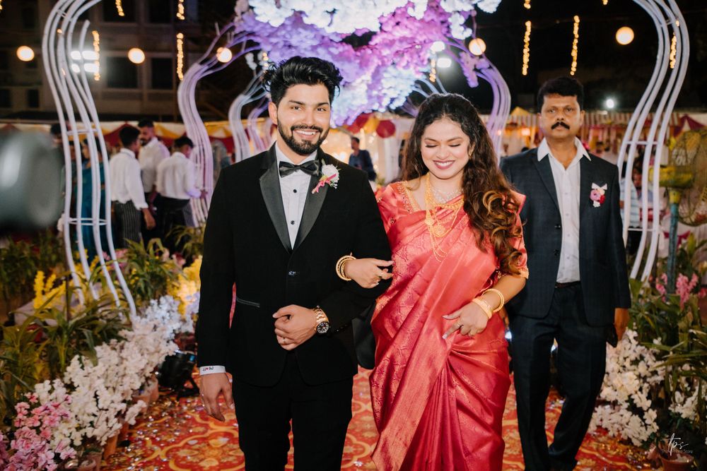 A couple walks down a decorated aisle with purple flowers and lights at an elegant wedding ceremony.
