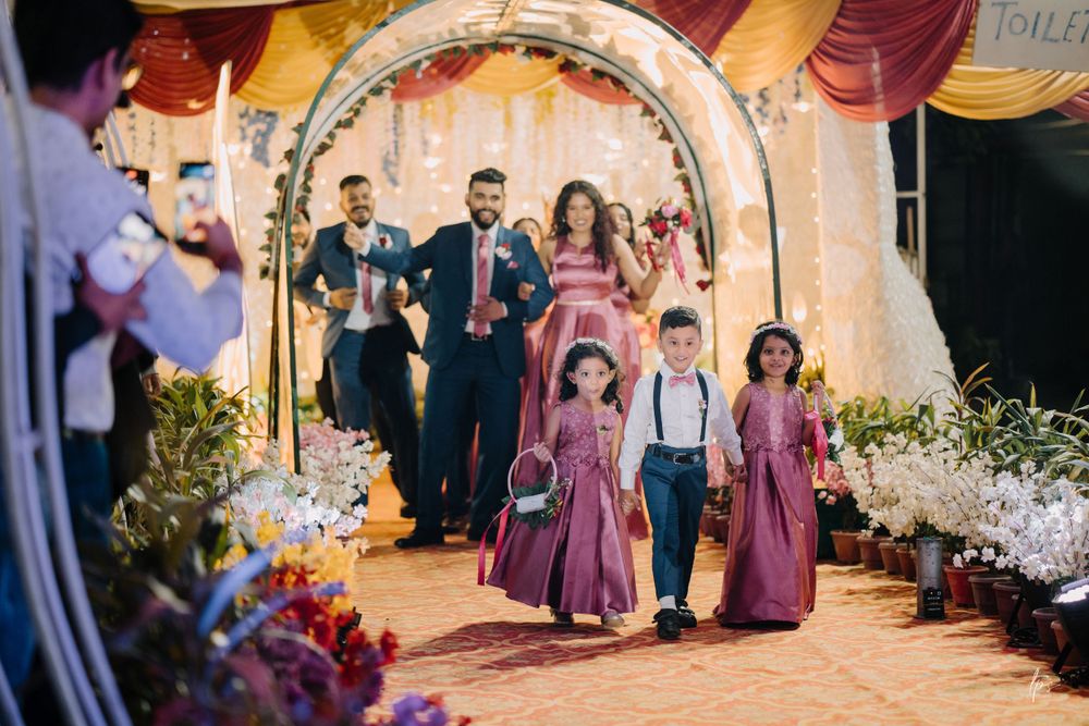 Wedding party walks through a floral archway decorated with purple and gold drapes.