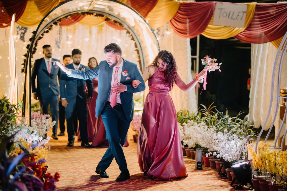 Wedding celebration with guests dancing under an illuminated archway with burgundy decor.