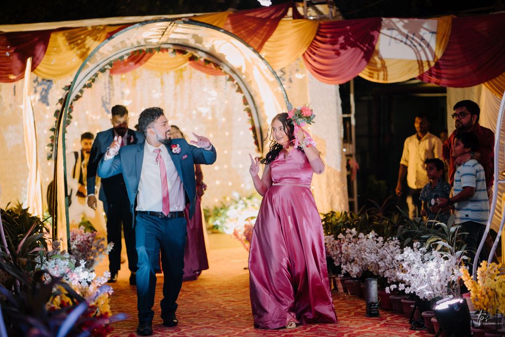 Wedding guests dancing and celebrating under a decorated arch with festive lighting.