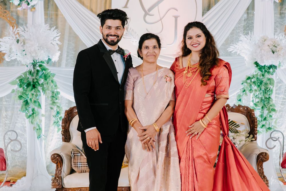Three people pose in formal attire against an elegant floral backdrop at a wedding celebration.